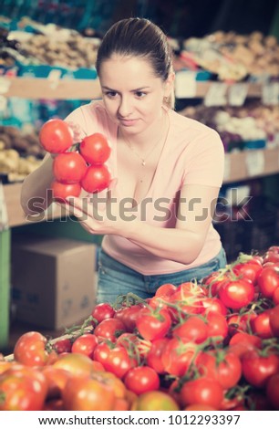 Young woman looking for fresh tomatoes in vegetable store
