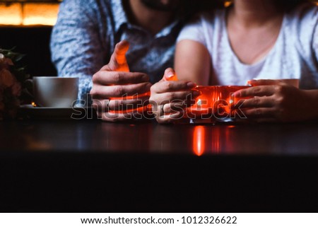 Husband and wife sitting at the table, holding hands and candles, wedding rings on fingers, hands on the table, cups of coffee on the table, bouquet, married people, couple in love, home