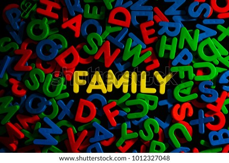Yellow plastic letters word FAMILY among colorful plastic letters on black background , family concept 