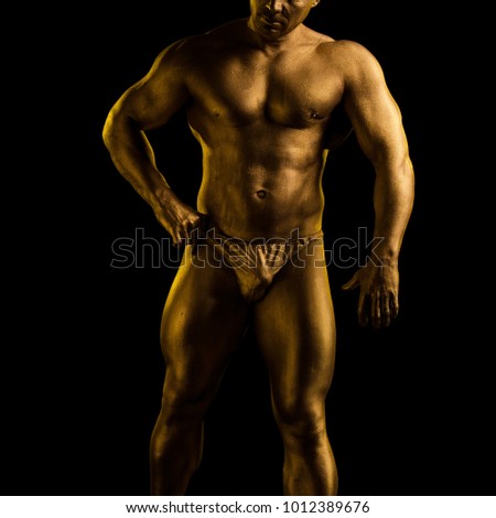 Male athlete bodybuilder in gold bodyart paint posing on black background