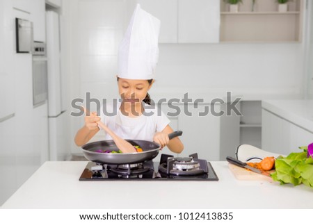 Picture of little girl wearing apron and hat while cooking healthy meal in the kitchen