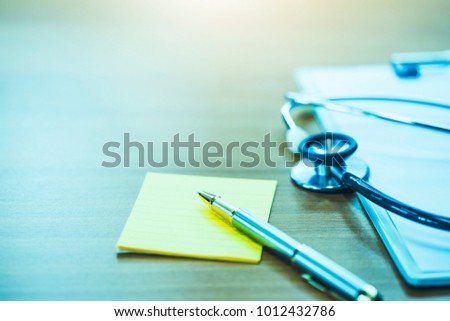 pen on yellow note paper and Stethoscope over paper clipboard    on doctor table or office, medical class or knowledge.