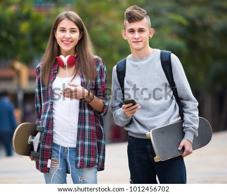 Portrait of cheerful girl and boy teenagers walking with skateboards outdoors 
