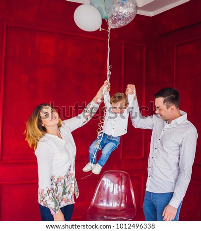 Beautiful young family and their little son pose with balloons in a cosy room