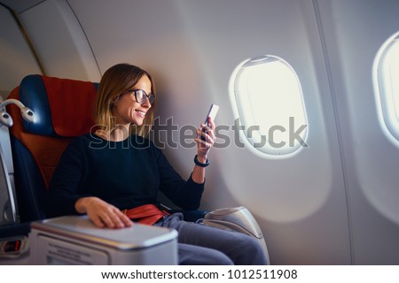 Traveling and technology. Flying at first class. Pretty young businees woman using smartphone while sitting in airplane. Royalty-Free Stock Photo #1012511908