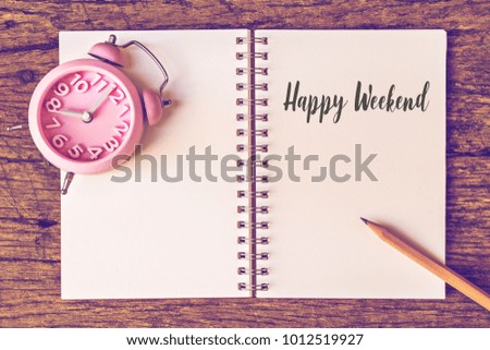 recycle paper notebook with Happy weekend text pink retro clock on wooden table.top view image. 