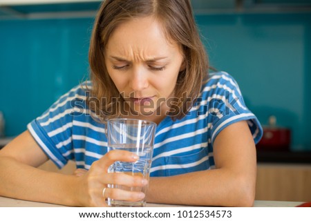 Dissatisfied Woman Looking into Glass of Water Royalty-Free Stock Photo #1012534573