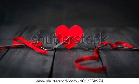 Red paper hearts and a fork with a ribbon. Dark wooden background. Copy space. St. Valentine's Day. Greeting card.