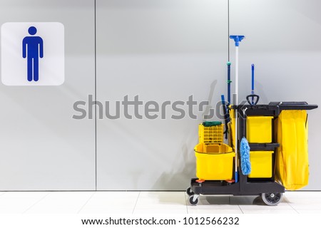 Yellow mop bucket and set of cleaning equipment and sign of men toilet on the wall in the airport