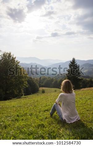 Girl on hiking trip enjoying the sunset view from above. Girl relax and refresh on mountain background is a landscape of high mountains, white clouds. Girl on the mountain looking at the sunny sky