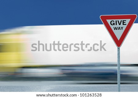 Give way yield road traffic sign and motion blurred truck in the background, blue sky