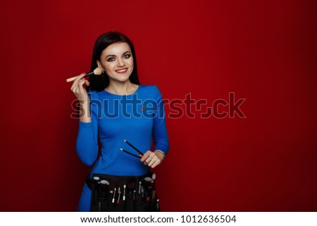portrait of the professional makeup artist. bright picture of smiley brunette woman with make-up brushes on a red background