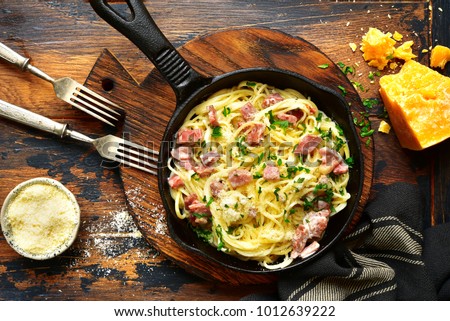 Traditional italian dish spaghetti carbonara with bacon in a cream sauce in a skillet over dark wooden background.Top view with copy space. Royalty-Free Stock Photo #1012639222
