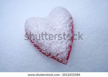 Single red heart covered with snow liying on white fluffy cold snow. Lost love.