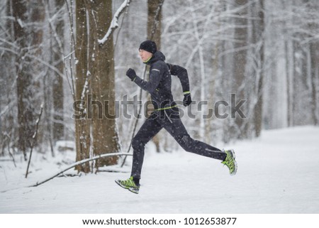 Photo from side of man in sports clothes on run in winter forest