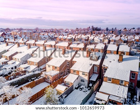Aerial view of snow covered traditional housing suburbs in England. Snow, ice and adverse weather conditions bring things to a stand still in the housing estates of a British suburb Royalty-Free Stock Photo #1012659973