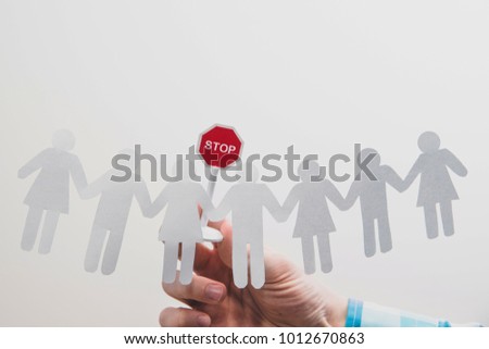 Hand holding a stop sign over one of the people in the crowd. Characters cut from paper. The boss or superior orders to stop the bad practices. Warns the employee against bad work. Royalty-Free Stock Photo #1012670863