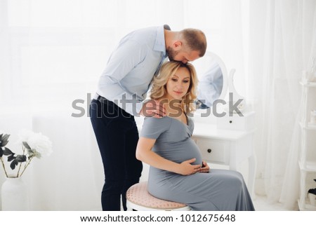 Beautiful couple handsome man and pregnant woman in long gray dress holding smart phone and taking self portrait. Romantic family mom and dad expaacting child, macking photo together.