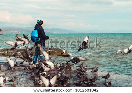 the guy is standing by the sea. many birds. feeds. vacation and travel