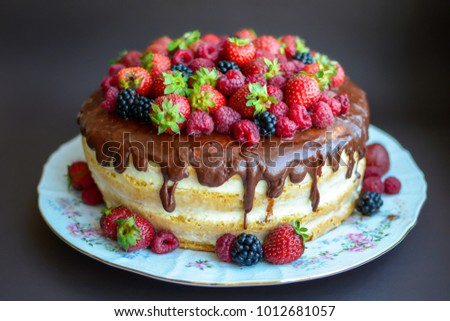 Cake in chocolate icing with fresh strawberries, raspberries and blackberry on a dark background. Close-up. Picture for a menu or a confectionery catalog.