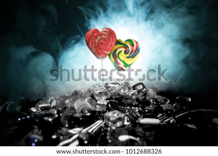 Few colorful candy heart lollipops on different colored candies against dark toned foggy background. Selective focus