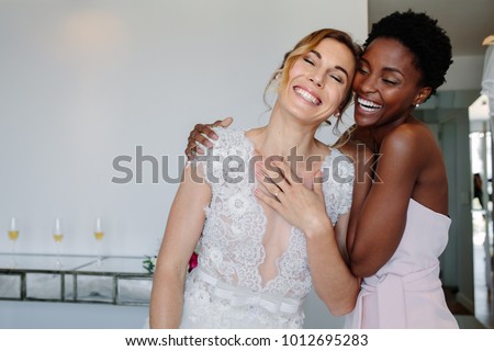 Gorgeous bride in wedding gown having fun with bridesmaid in hotel room. Cheerful bride and bridesmaid on the wedding day. Royalty-Free Stock Photo #1012695283