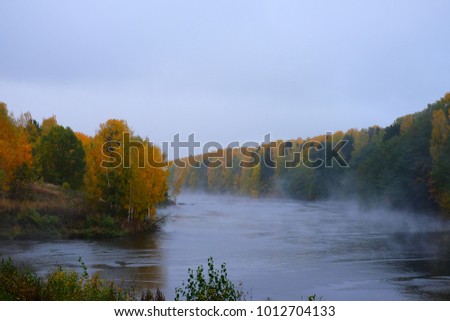 Beautiful views of the autumn landscape in the forest. The forest begins to be covered with yellow leaves, the river flows through the forest, over the river rises a fog.