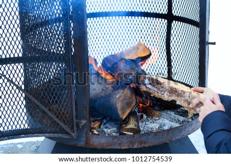 Outdoor metallic fireplace in winter season charged with firewood, in the burning process. Wood-burning fire pit with removable fire pan and with wide bar ribs and handles. Winter outdoor activity.