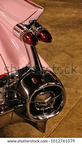 Tail fins and massive chrome details with pink paint on a classic american car.