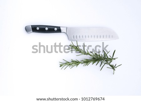 A kitchen knife with some fresh cut rosemary on a white background. 