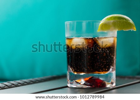 Cold drink in a glass with ice, with a slice of lime on the side of the glass with with water dripping down the side of the glass on a blue background