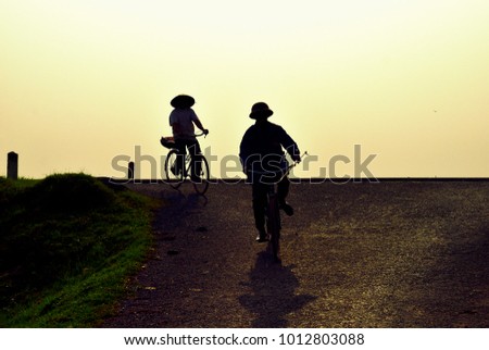 Silhouette of two Vietnamese people rides a bike at sunset