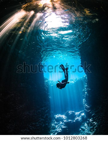 Girl diving in cavern with lightbeams coming on top of her Royalty-Free Stock Photo #1012803268