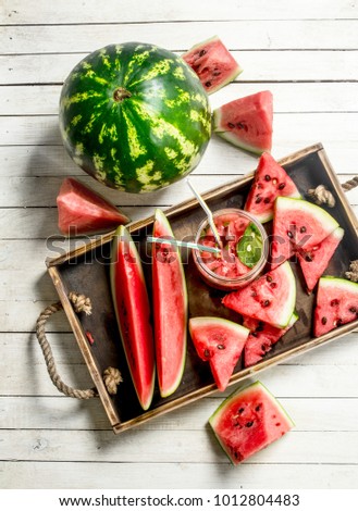 Watermelon juice in glass jar on a tray with slices of watermelon. On a white wooden table.