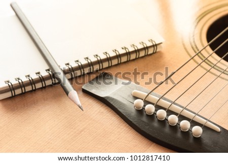 pencil and blank notebook on acoustic guitar in vintage tone. creative idea with music concept.