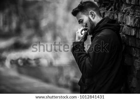 Vape man. Photo of a handsome young white guy with modern haircut in the black clothes vaping and letting off steam from an electronic cigarette near