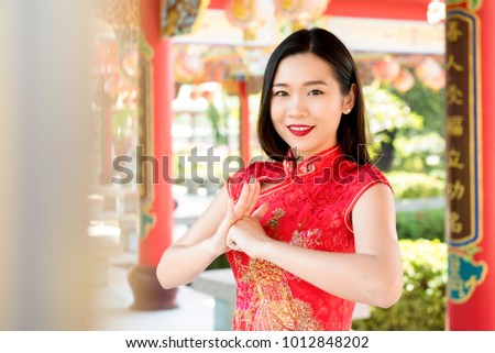Smiling  beautiful Asian woman in traditional red cheongsam qipao dress making salute in Chinese temple