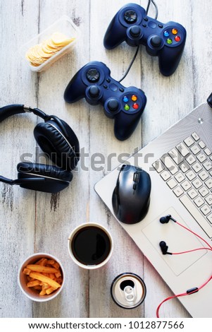 Top view of gamer background. Gamepads, headphone, laptop with mouse pad and snacks over white table.
