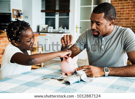 Dad and daughter saving money to piggy bank Royalty-Free Stock Photo #1012887124