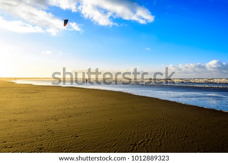 Early morning at beach with kite surfers against blue sky with puffy clouds.