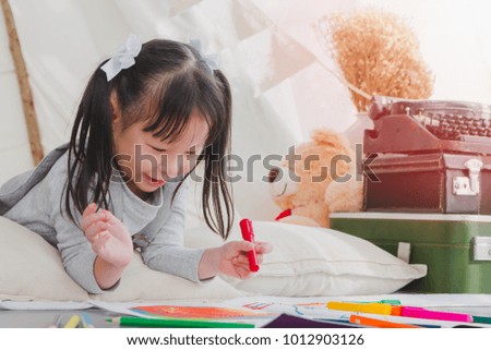 Happy Asian little cute girl drawing and painting color on notebook in a white room background.