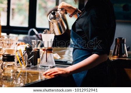 Women Barista to make a drip brewing, filtered coffee, or pour-over is a method which involves pouring water over roasted, ground coffee beans contained in a filter. in a coffee shop.vintage tone. Royalty-Free Stock Photo #1012952941