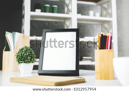 Close up of clean picture frame placed on office desk with coffee cup, supplies and other items on blurry background. Mock up 