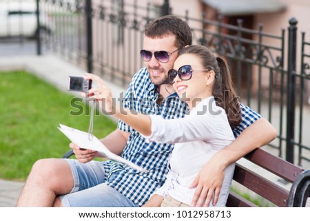 Traveling  Concepts. Young Caucasian Couple in Love Sitting on Bench Outdoors While Taking Selfie Pictures.Horizontal image Orientation