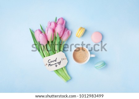 Beautiful breakfast on Mothers or Womans day. Coffee cup with pink tulip flowers, macaroon and note good morning on blue table top view. 