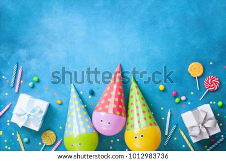 Birthday background with funny balloons in caps, gifts, confetti, candy and candles. Flat lay. Greeting card with copy space.