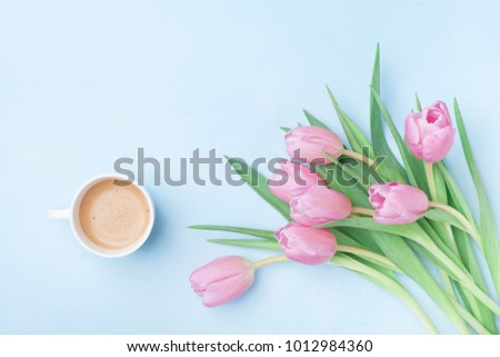 Beautiful spring breakfast on Mothers or Womans day. Bouquet of pink tulips and coffee cup on blue pastel table top view. Flat lay.