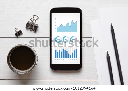 Graphs and charts elements on smart phone screen with office objects on white wooden table. All screen content is designed by me. Flat lay