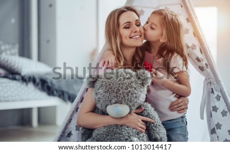 Attractive young woman with little cute girl are having fun together at home. Mom and daughter are sitting on the floor, hugging, kissing and smiling. Happy family concept. Mother's day.