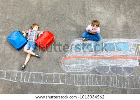 Two little kids boys having fun with train picture drawing with colorful chalks on asphalt. Children having fun with chalk and crayon painting. going on vacations and travel. Friends with suitcases.